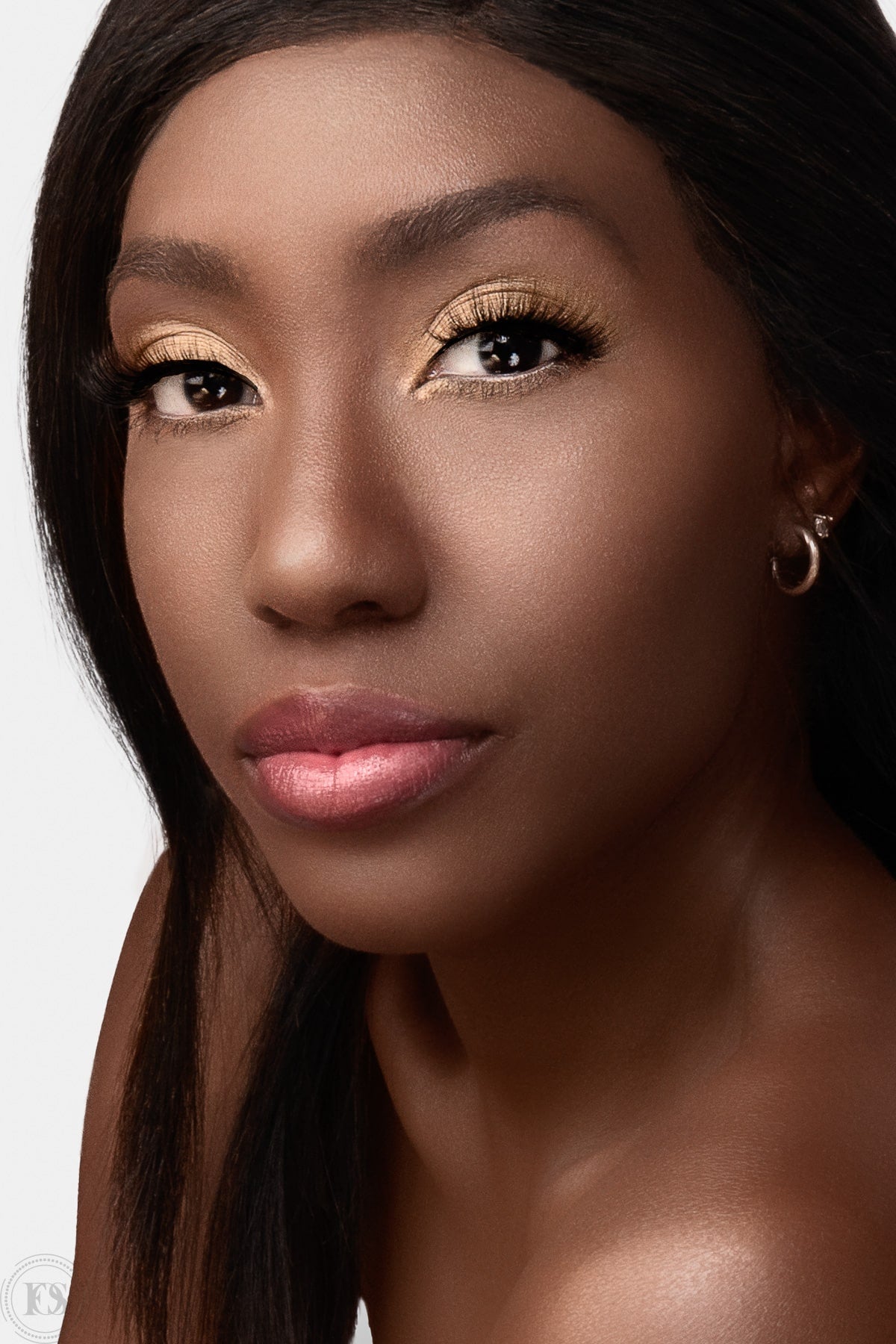 Närbild på kvinna med elegant makeup och fylliga lösögonfransar i guldtonad ögonskugga och mjukt rosa läppar, som framhäver en naturligt glamorös look.