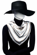Mannequin i svart hatt och polotröja bär en elegant scarf med diagonala ränder i vitt, svart, beige och brunt, knuten löst runt halsen.