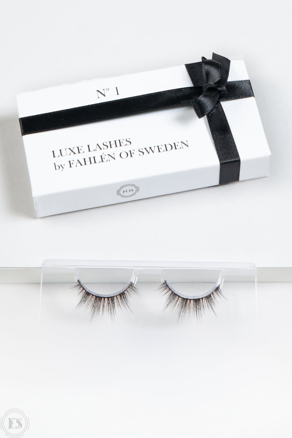 Elegant förpackning med texten “Luxe Lashes by Fahlén of Sweden” och en svart sidenrosett, placerad ovanför ett par fylliga, naturligt formade lösögonfransar i en transparent hållare.